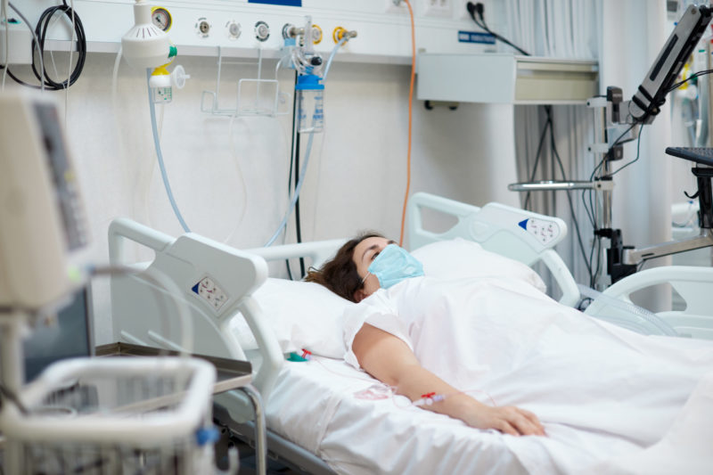 Hospital COVID patient with an oxygen mask lying down in bed